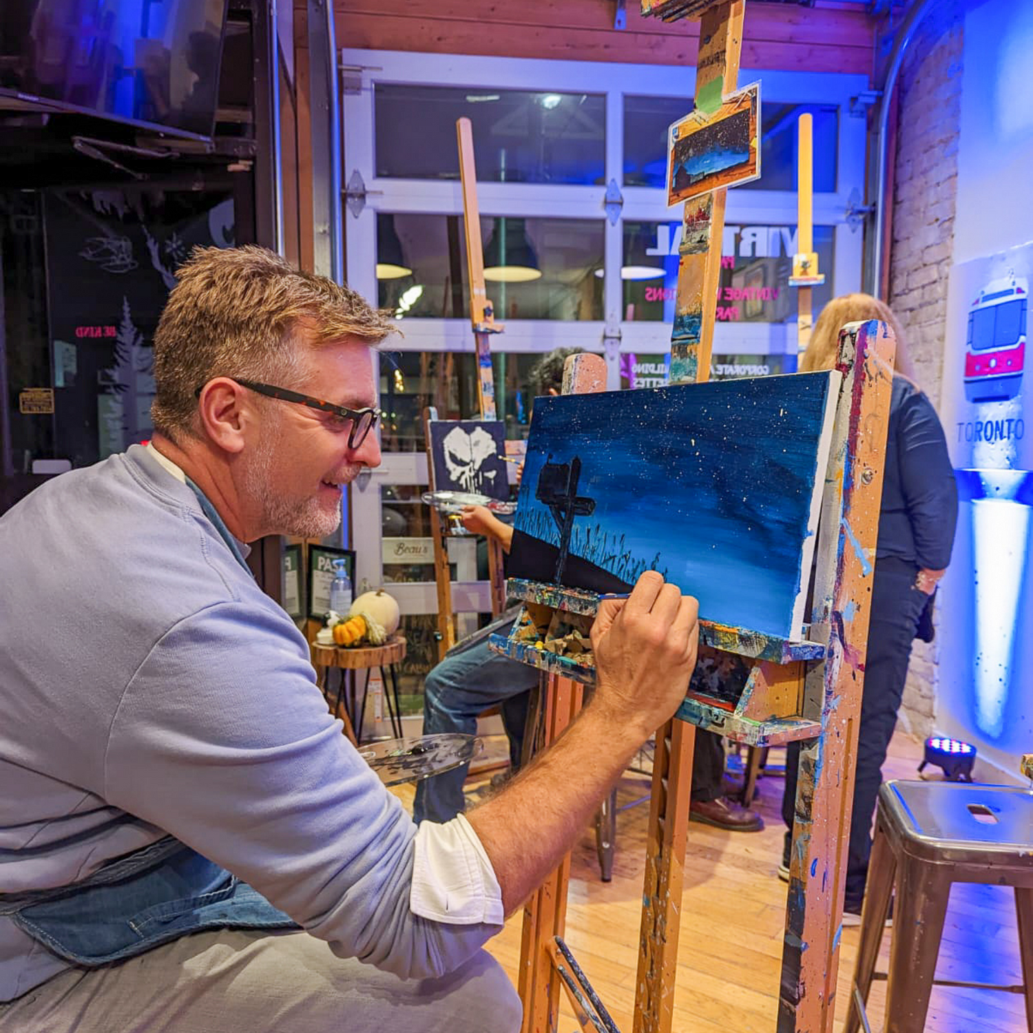 Man smiling and painting during team building paint night activity at Paint Cabin