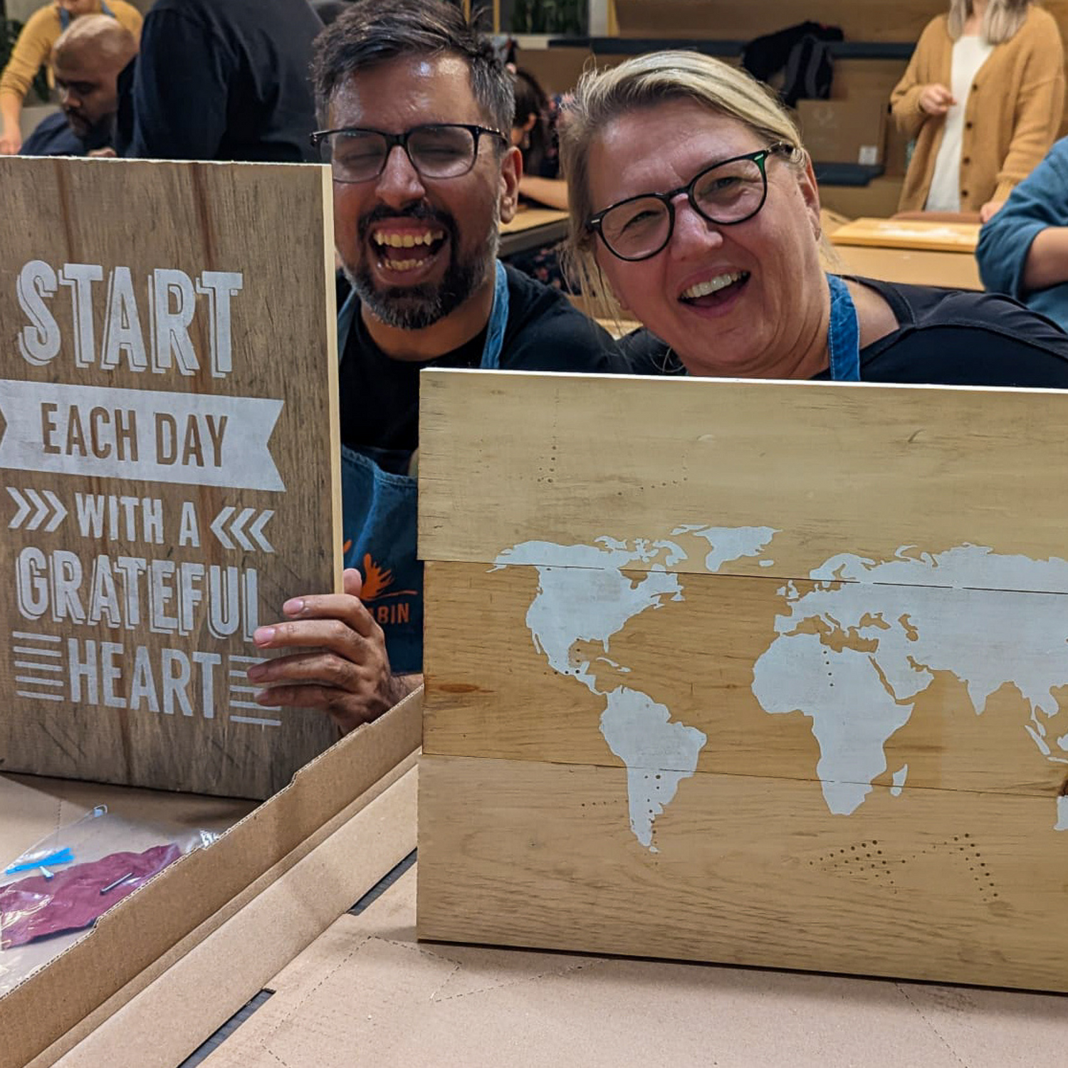 Two team members smiling and showcasing their finished projects during an Employee engagement team event with Paint Cabin