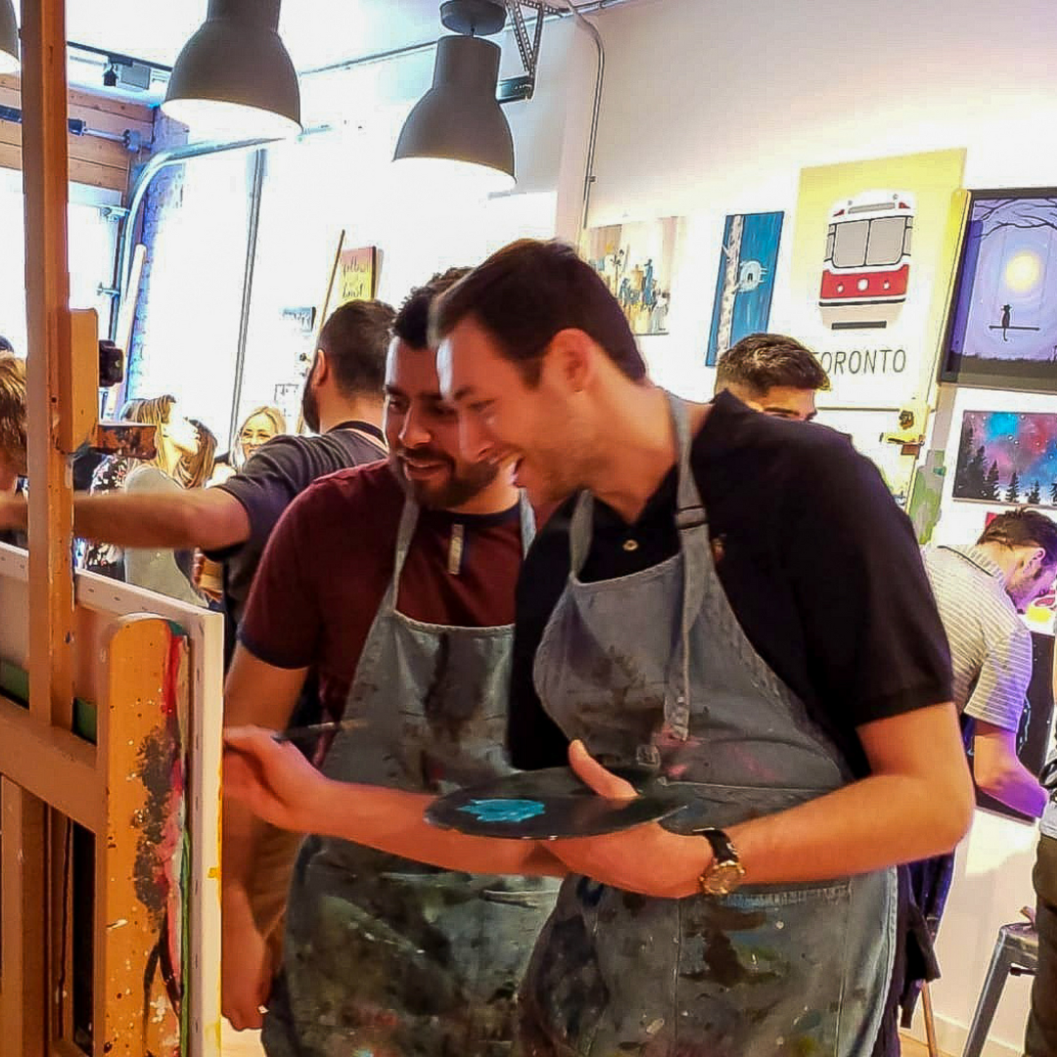 Two guys laughing and painting during a Paint Cabin employee engagement event